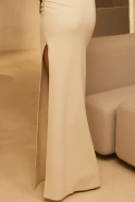 Elegante - asymetryczna sukienka maxi w kolorze ecru z broszką z piór